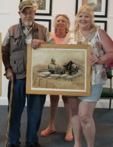 Man and two women holding a picture of 2 soldiers in a fox hole
